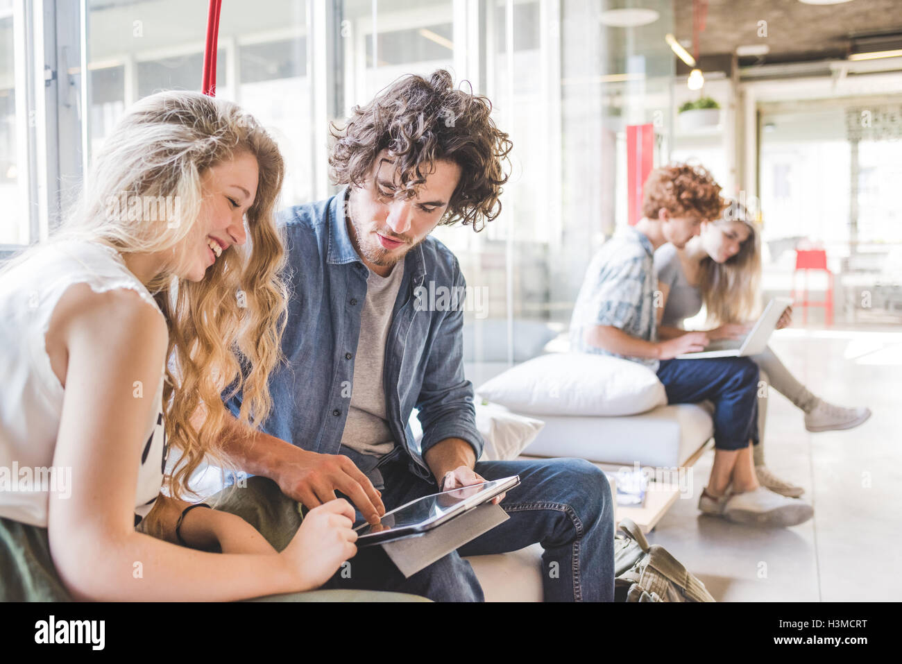 Co-lavoratori che operano sul computer portatile sul divano dalla finestra Foto Stock