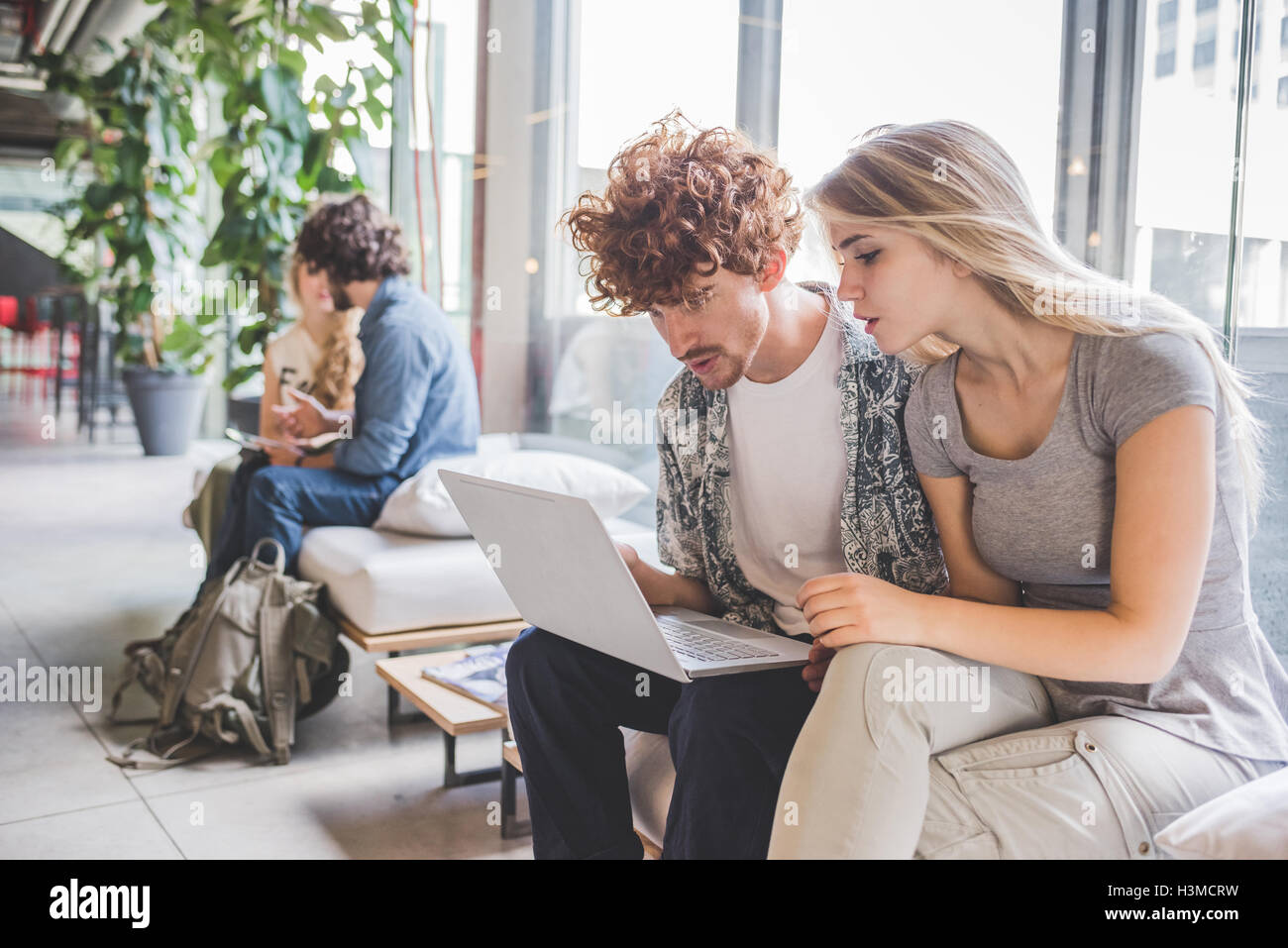 Co-lavoratori che operano sul computer portatile sul divano dalla finestra Foto Stock