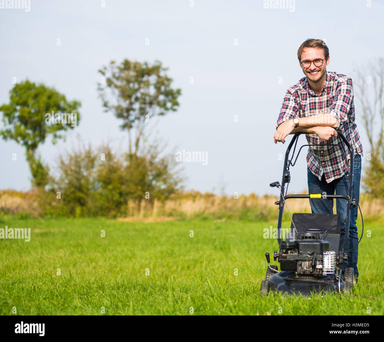 Uomo che falcia l'erba alta con il tagliaerba a benzina in giardino o  cortile processo di taglio del prato con il tosaerba a mano