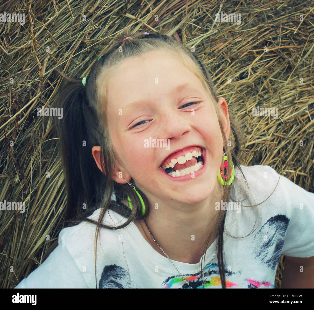 Giovane ragazza bionda sorridente scherzosamente durante la riproduzione sulla balla di fieno Foto Stock