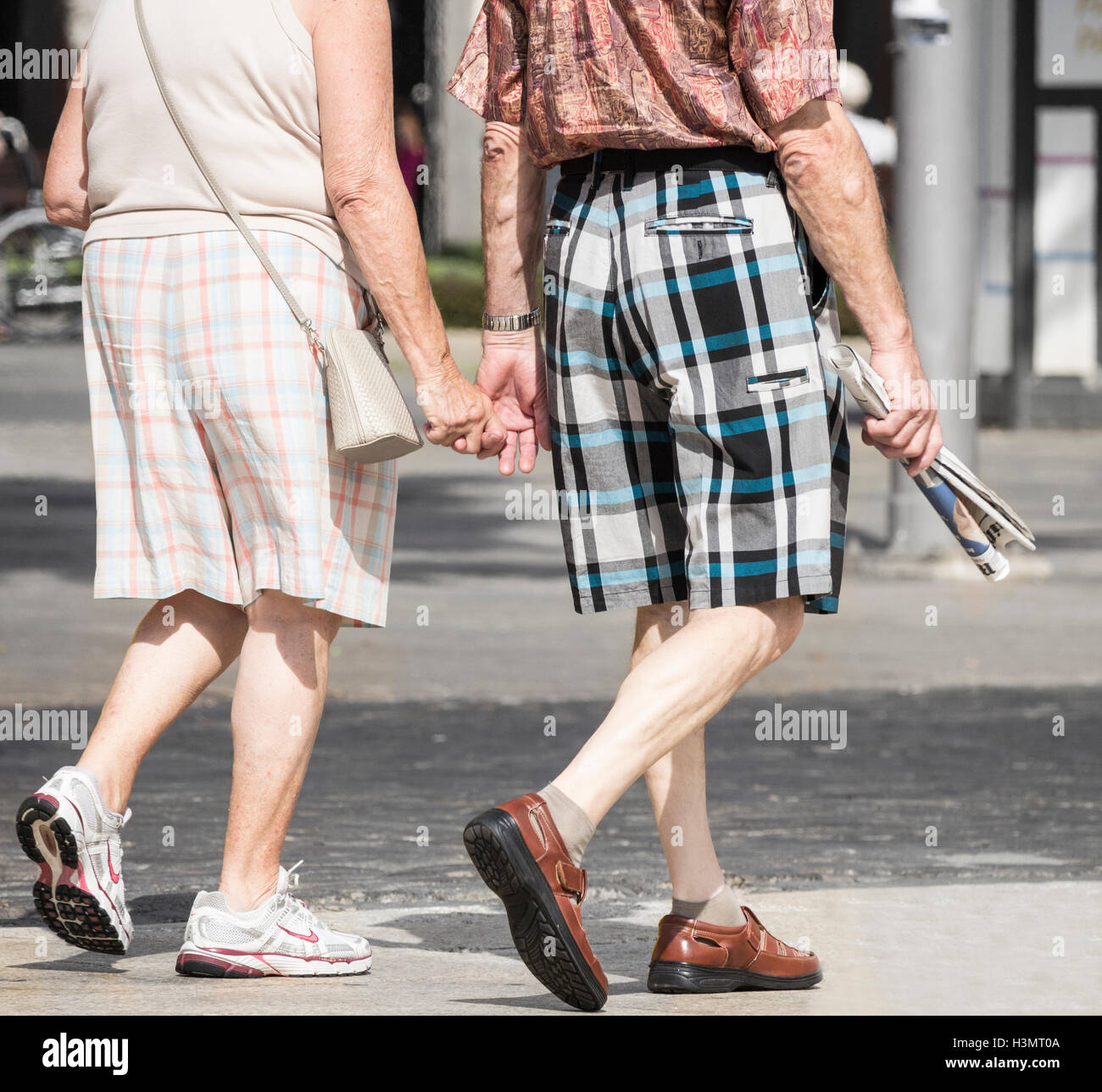 Coppia di anziani in pantaloncini controllato tenendo le mani in vacanza in Spagna. Uomo con copia del giornale inglese. Foto Stock