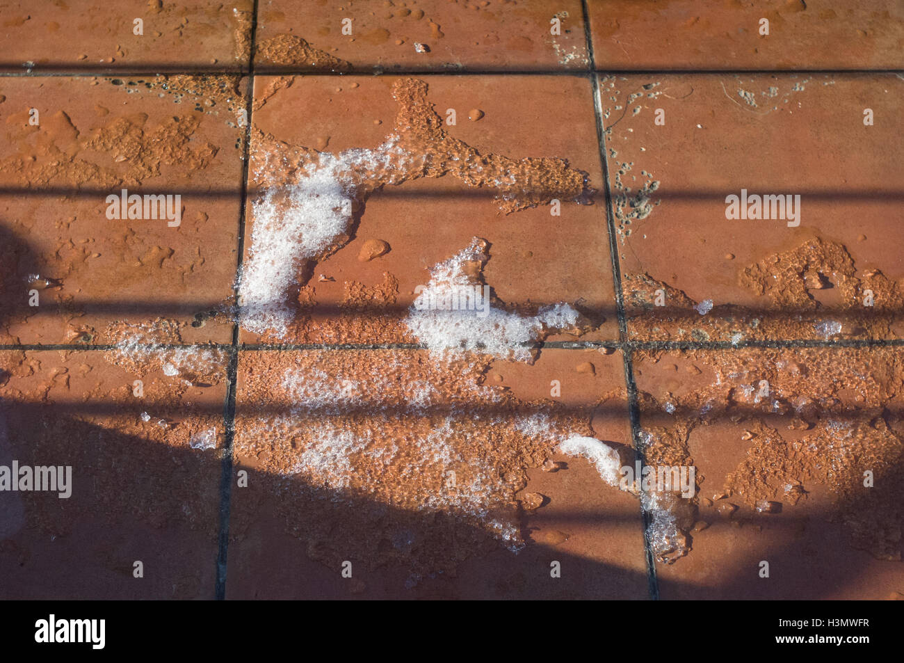 Il ghiaccio e la neve che si scioglie in luce del sole su piastrelle ceramiche di balcone Foto Stock