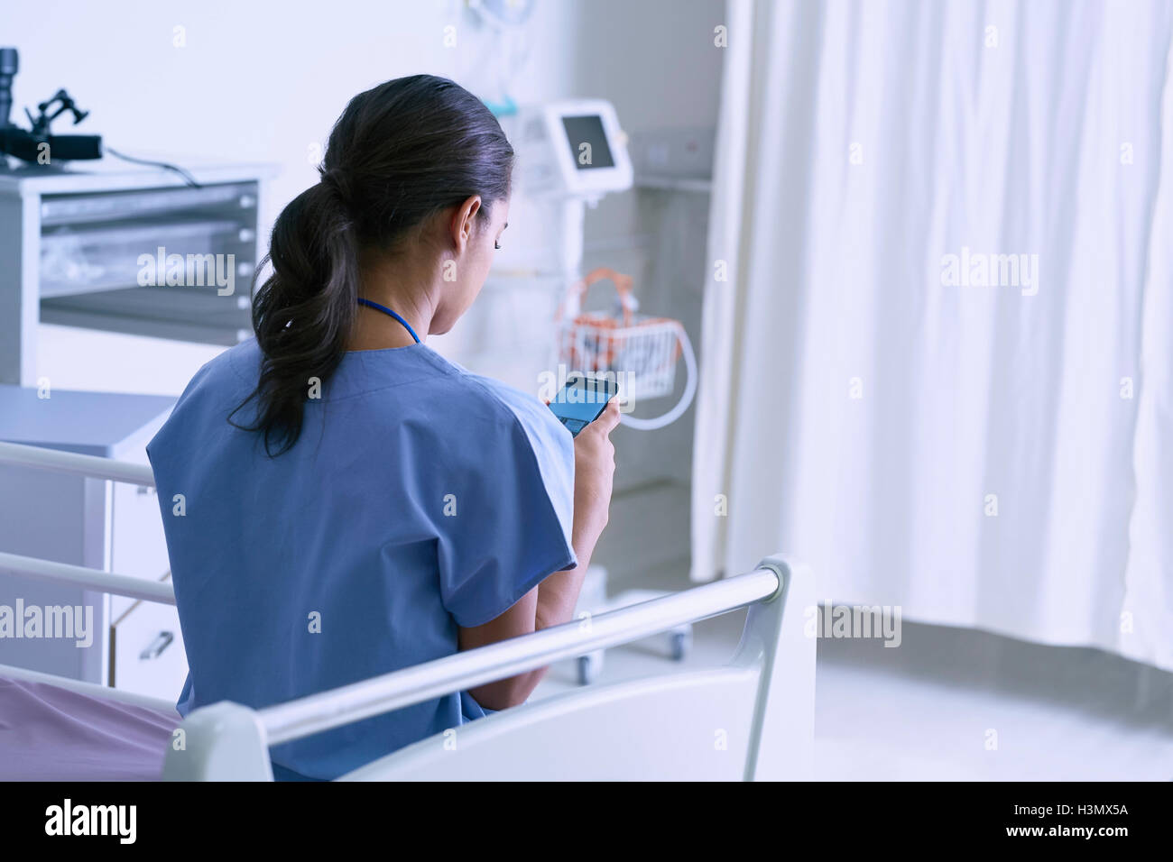 Medic femmina seduta sul letto di ospedale la lettura di testi dello smartphone Foto Stock
