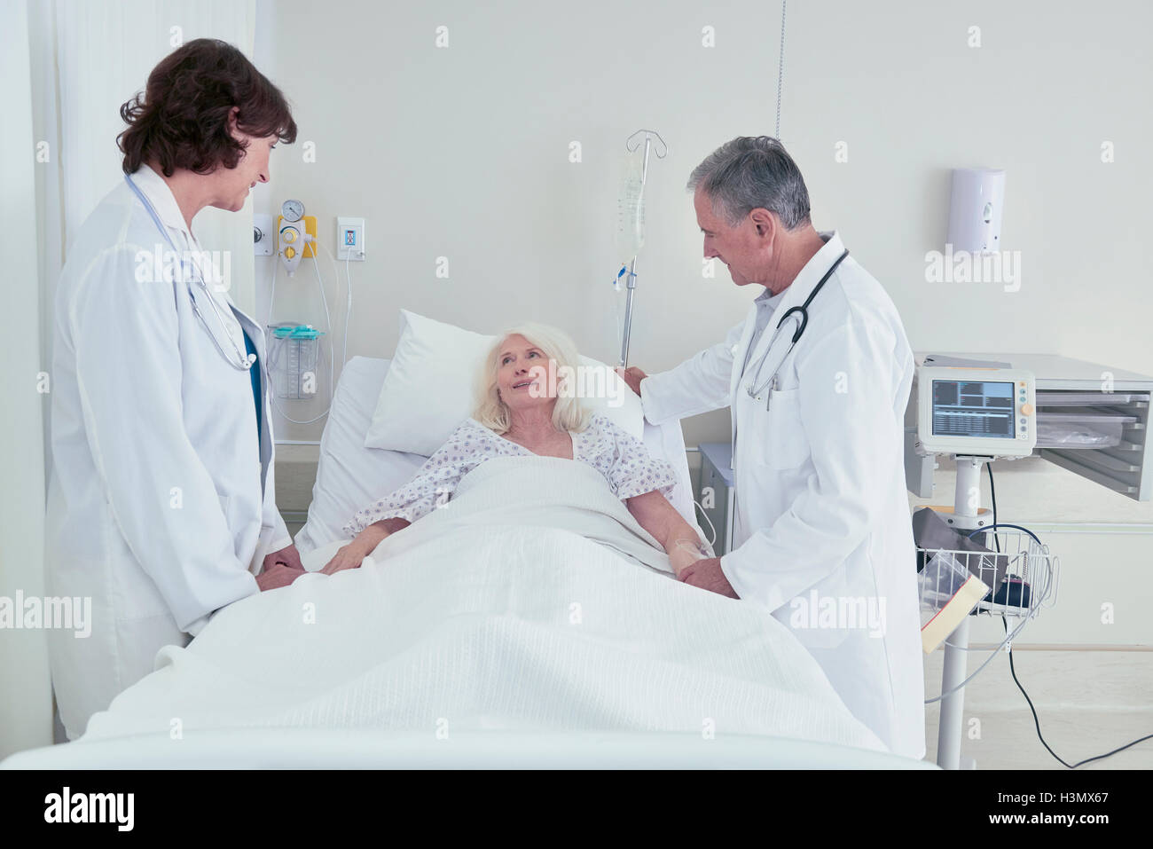 Due medici a parlare con il senior paziente di sesso femminile nel letto di ospedale Foto Stock