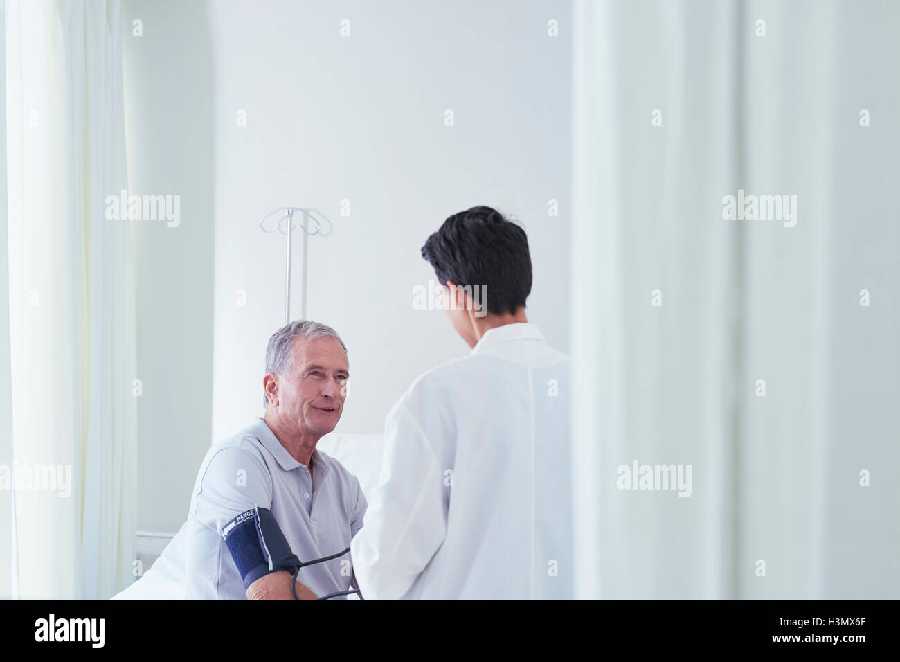 Senior paziente di sesso maschile avente la pressione del sangue sangue manometro presa dal medico donna Foto Stock