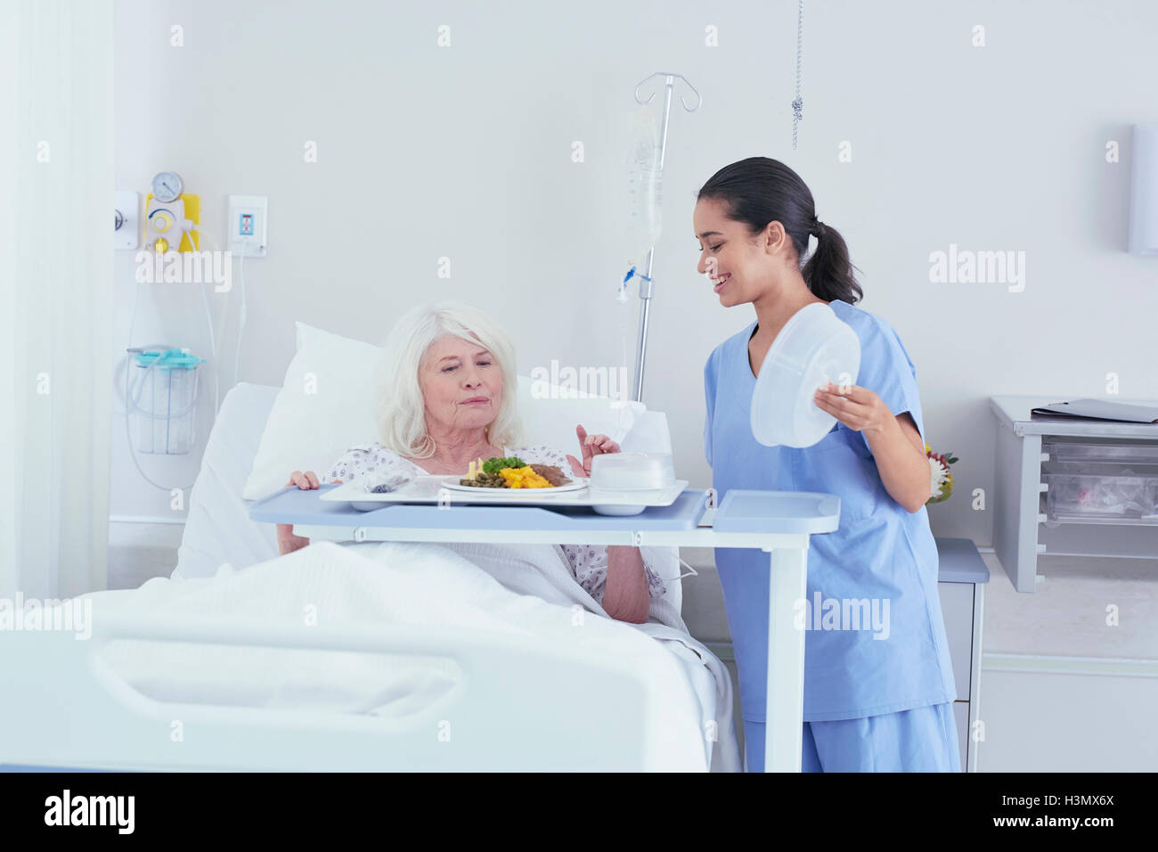 Un infermiere che serve il pranzo al senior paziente femmina nel letto di ospedale Foto Stock