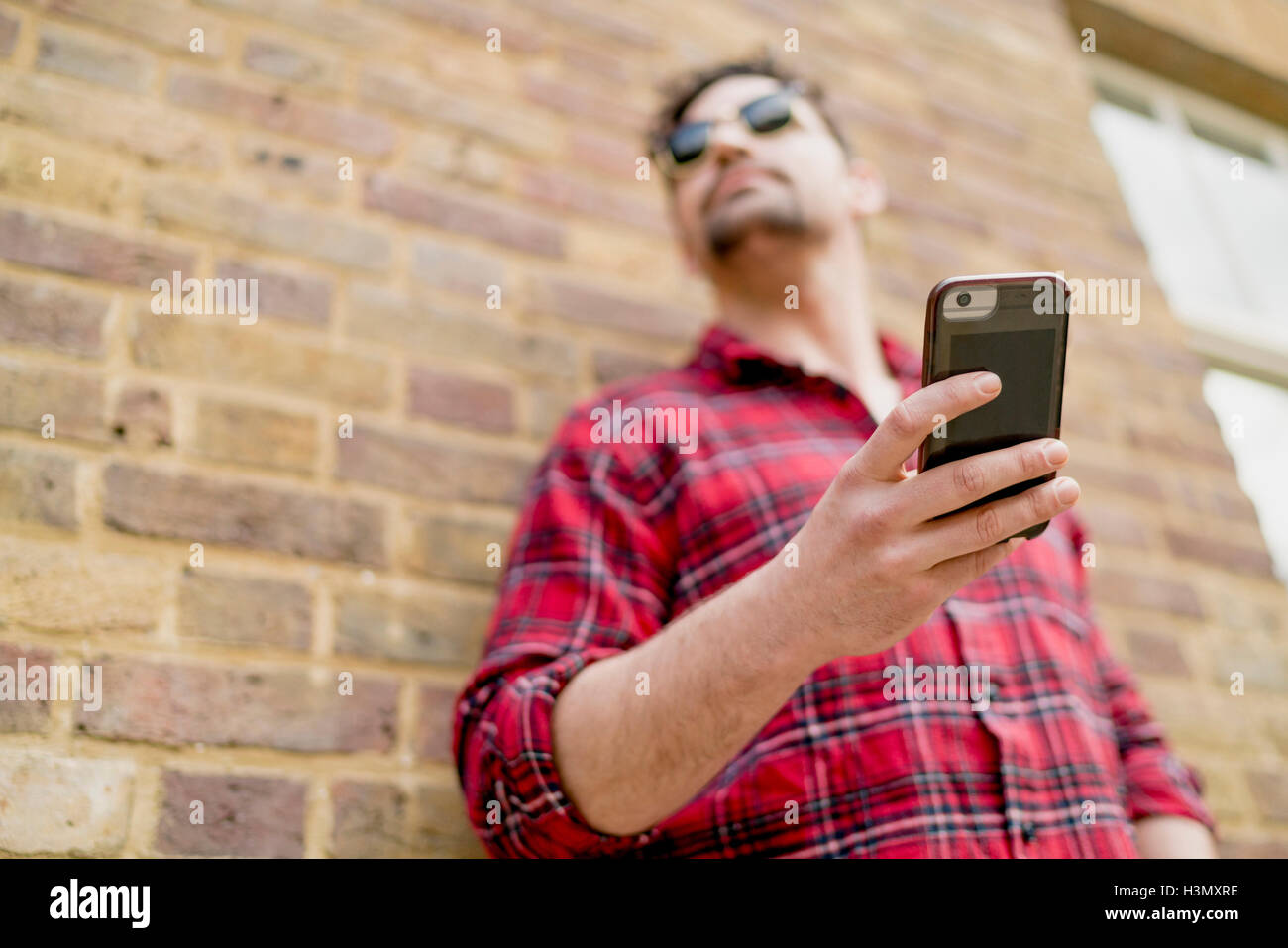 Basso angolo vista del giovane uomo appoggiato contro un muro di mattoni tenendo lo smartphone Foto Stock