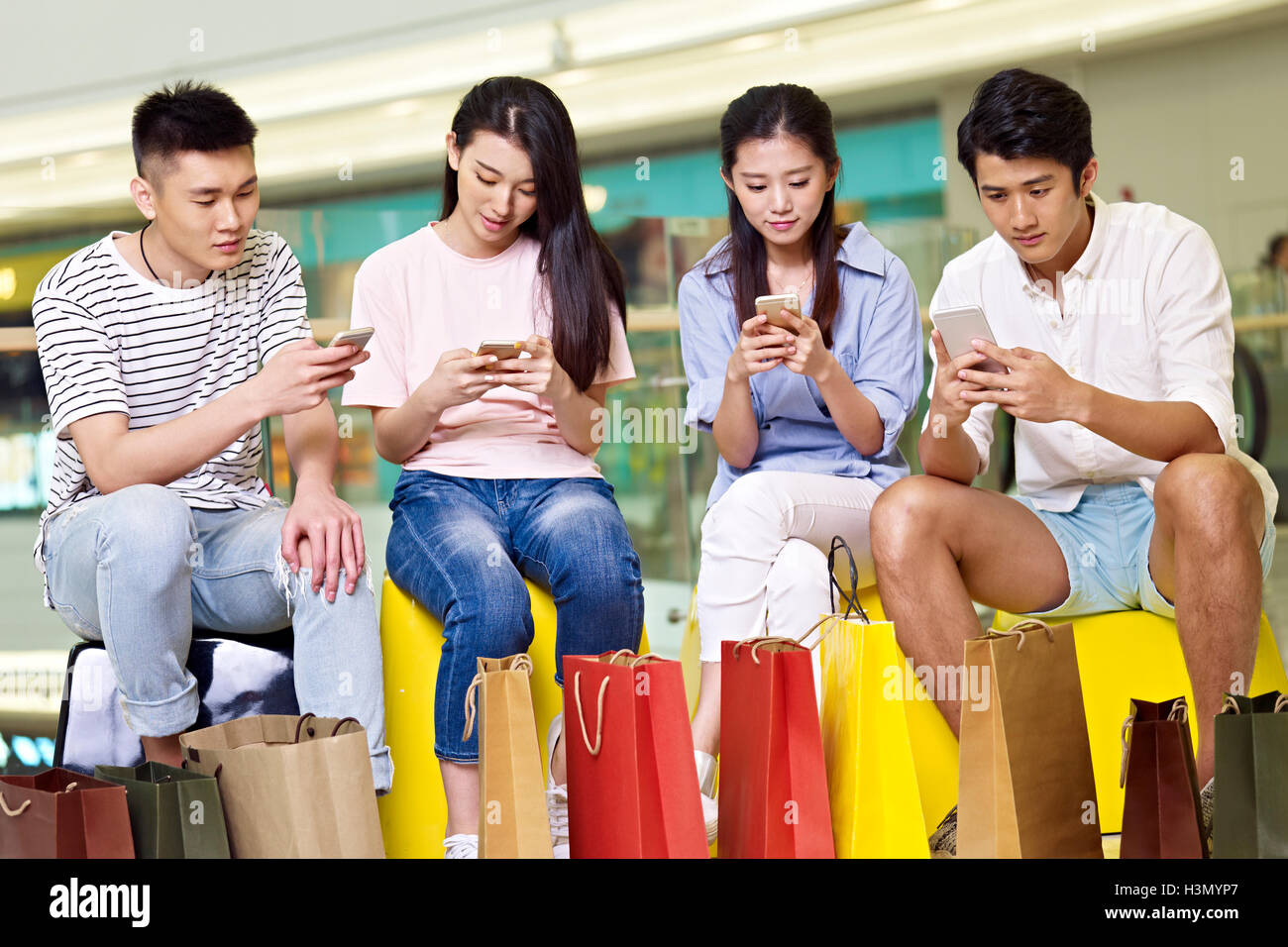Un gruppo di giovani popoli asiatici di uomini e donne a giocare con i telefoni cellulari mentre prendendo una pausa nel centro commerciale per lo shopping Foto Stock