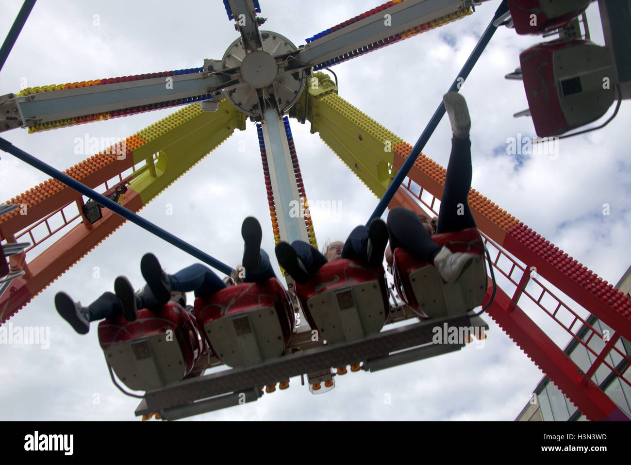Fairground Ride con persone di ragazzi e ragazze che viene sollevato e filate su un braccio di una corsa in alto nel cielo con Sfondo nuvola Foto Stock