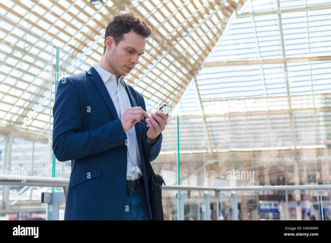 Imprenditore iscritto un messaggio sullo smartphone, stazione ferroviaria in attesa lounge in background Foto Stock