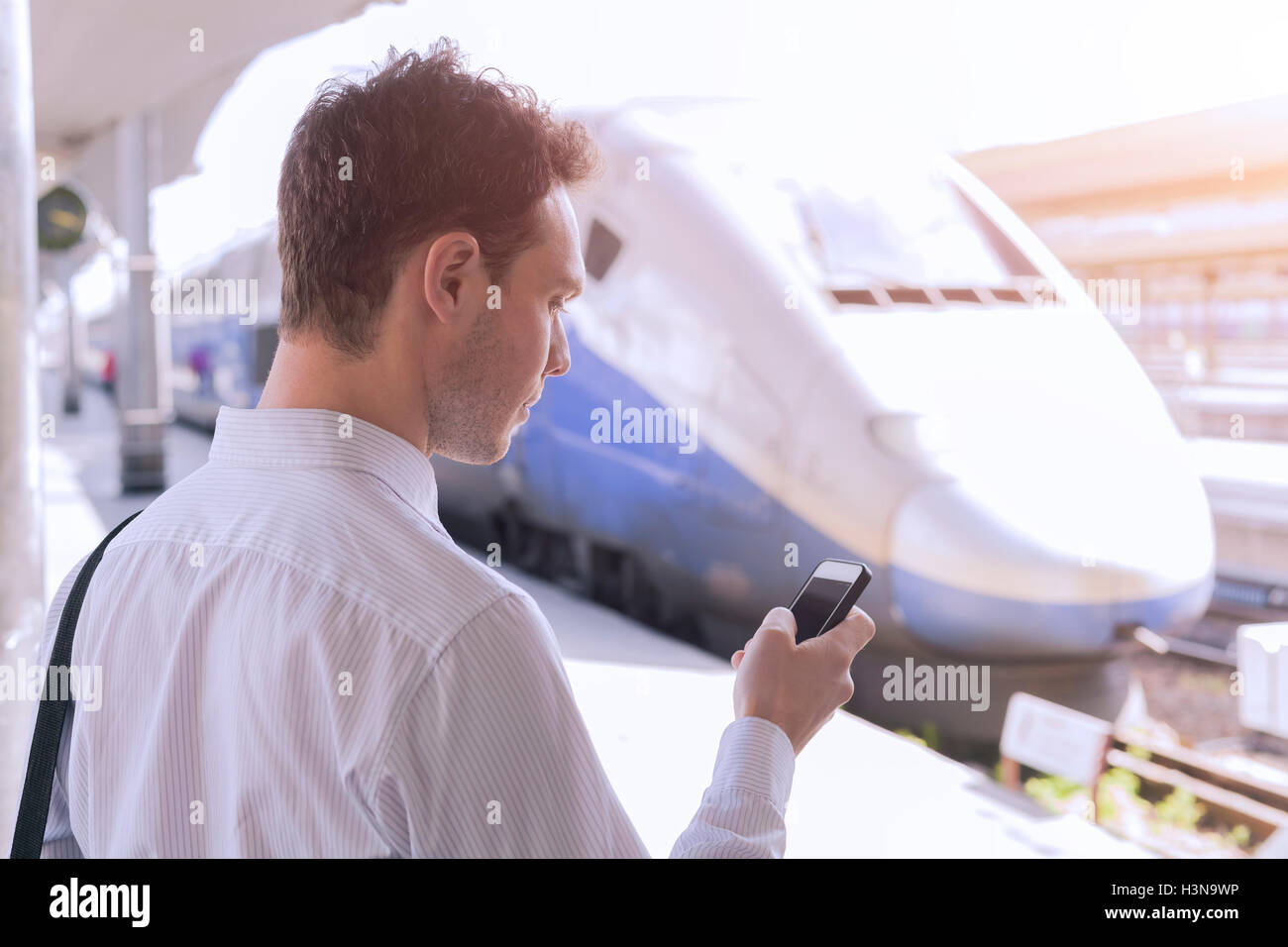 Giovani maschi adulti utilizzando app sullo smartphone durante un viaggio d'affari con il treno in background Foto Stock