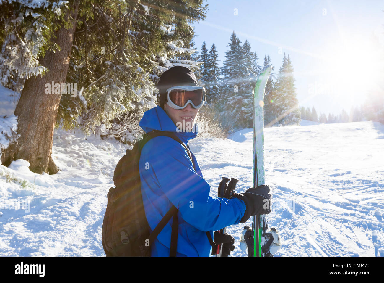 Sciatore sorridente in piedi vicino alla foresta con sci in mano, giornata di sole Foto Stock