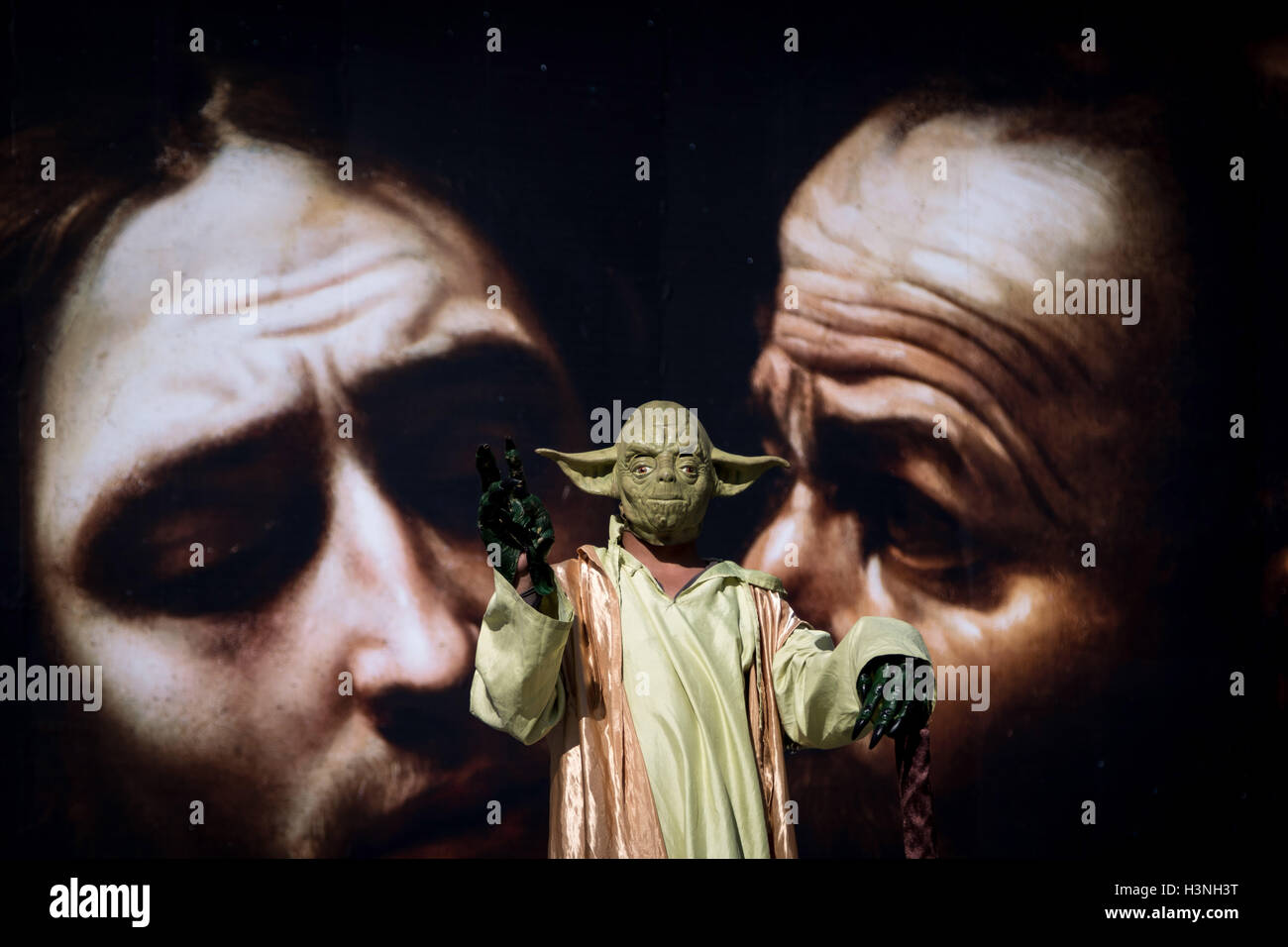 Londra, Regno Unito. 11 ottobre, 2016. Un galleggiante Yoda street performer nella parte anteriore di un grande poster di promozione " al di là " Caravaggio mostra al di fuori del National Gallery di Londra in Trafalgar Square. Credito: Guy Corbishley/Alamy Live News Foto Stock