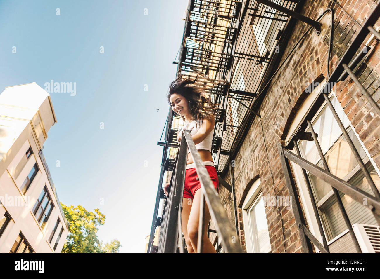 Donna climbing fire escape scala di edificio di appartamenti, Boston, MA, Stati Uniti d'America Foto Stock