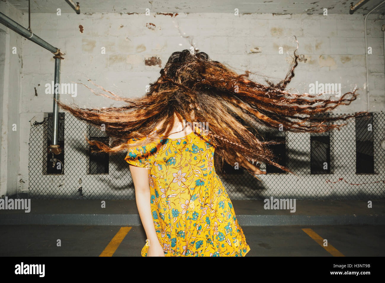Vista frontale della giovane donna scuotendo i suoi lunghi capelli ondulati nel parcheggio al coperto Foto Stock
