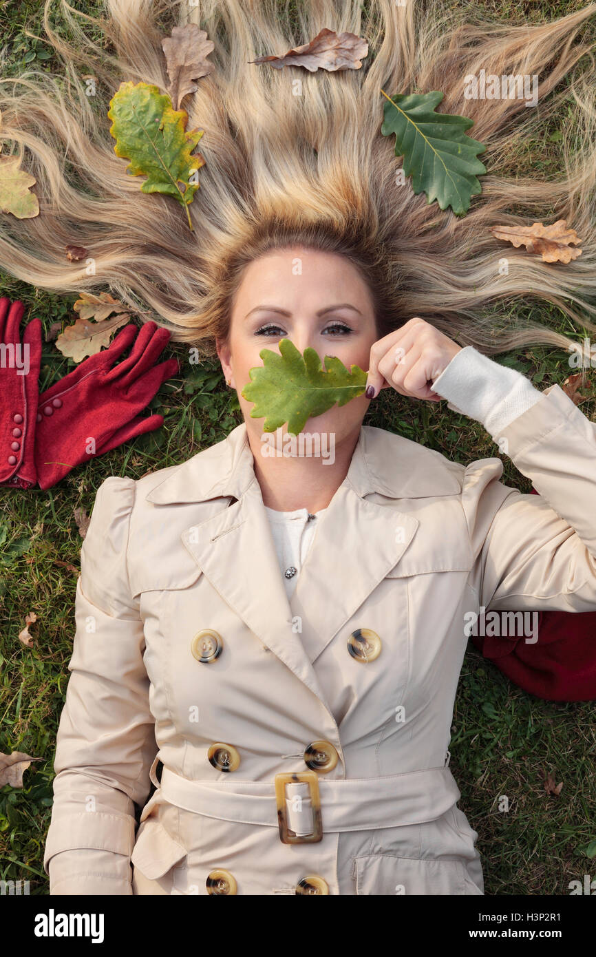 Donna sdraiata su un prato con il volto coperto con foglie Foto Stock