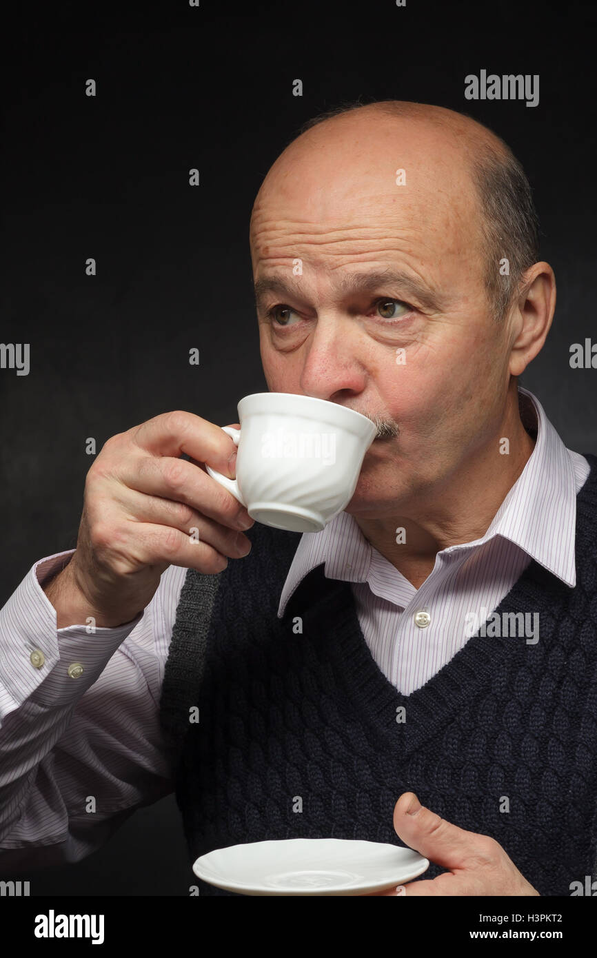 Anziani uomo calvo con un baffi beve un sorso di caffè da una tazza bianca. Foto Stock