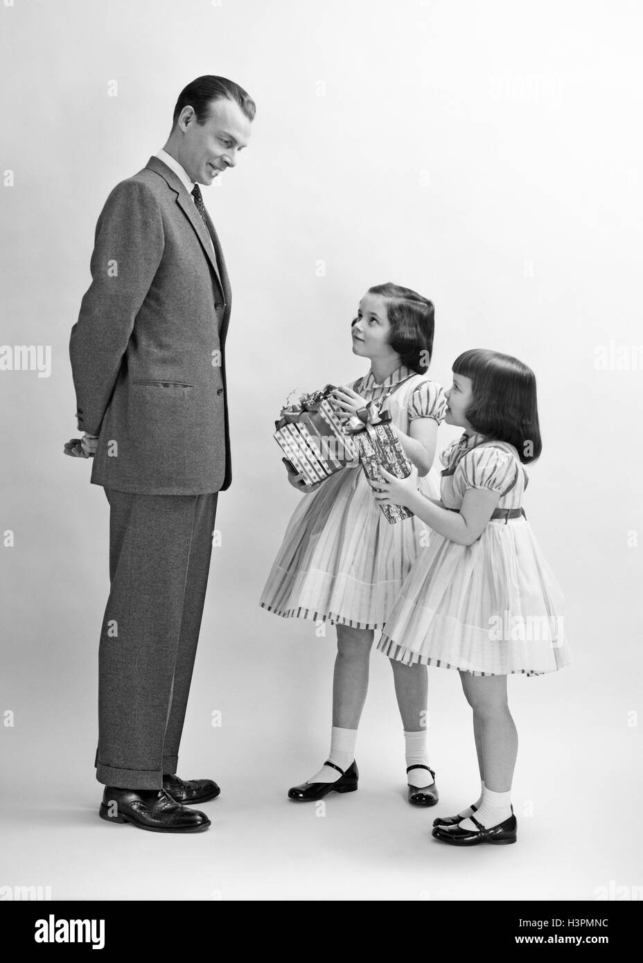 Anni Cinquanta il padre e due ragazze sorelle indossando abiti di corrispondenza tenendo i regali di Natale Foto Stock