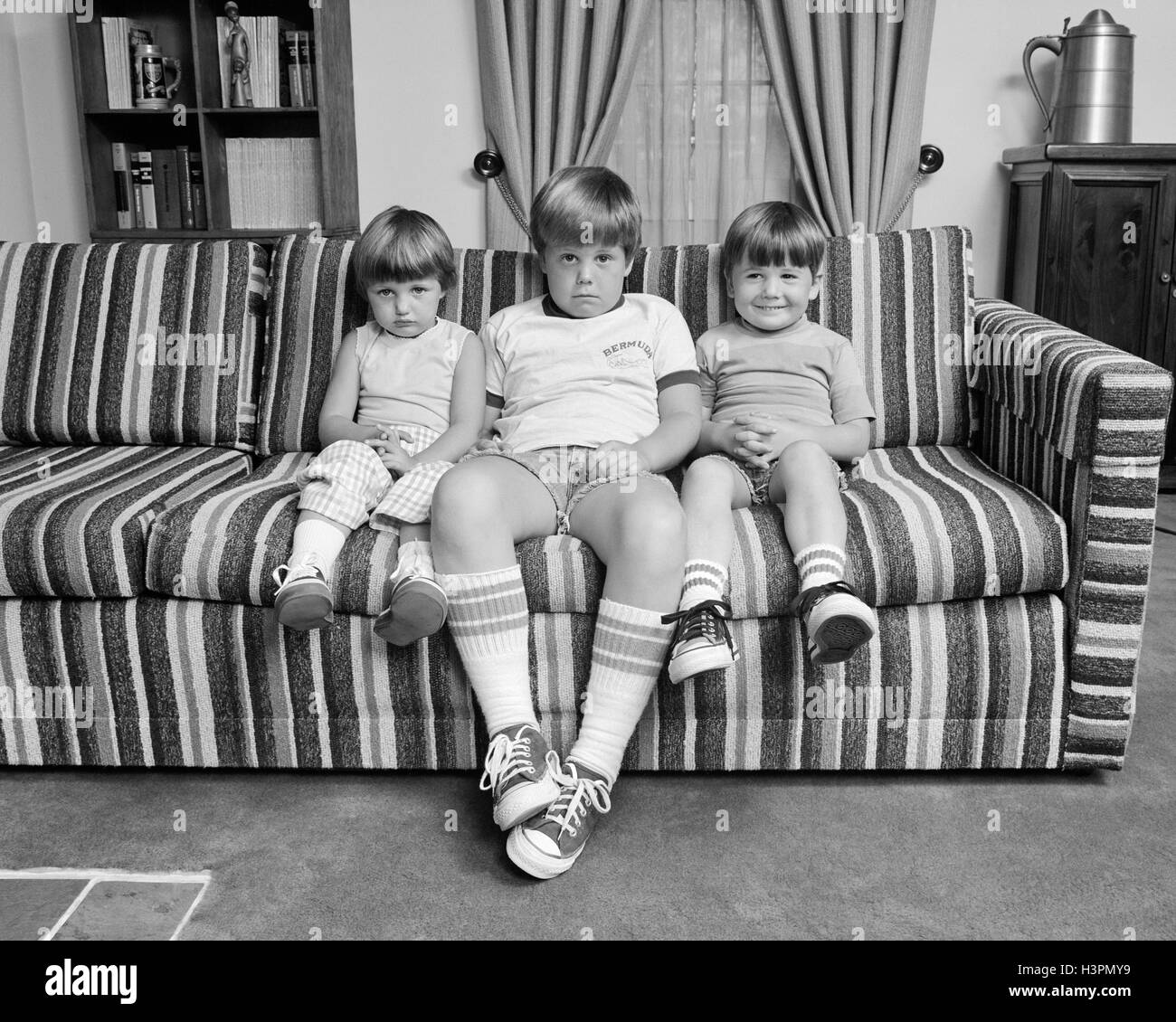 Anni Settanta tre fratelli seduti sul divano guardando in telecamera Foto Stock