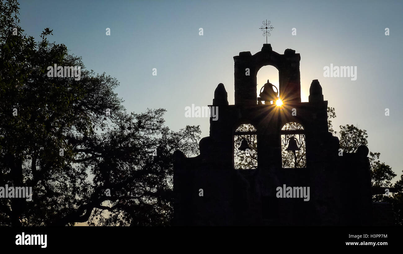 La missione spagnola Espada campane in silhouette come il sole tramonta dietro la missione di San Antonio, Texas Foto Stock