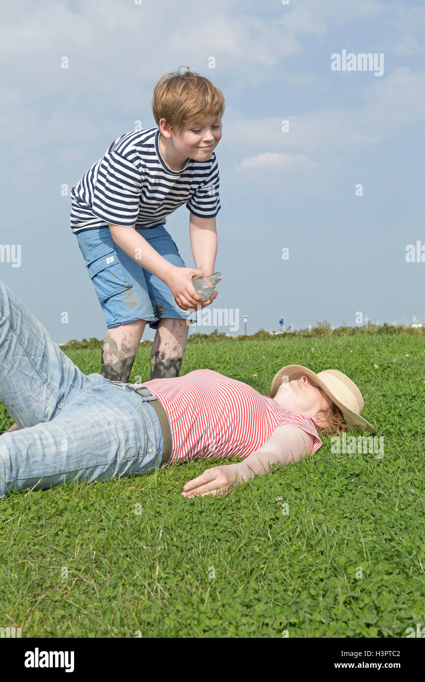 Ragazzo versando acqua sulla sua madre del sonno Foto Stock