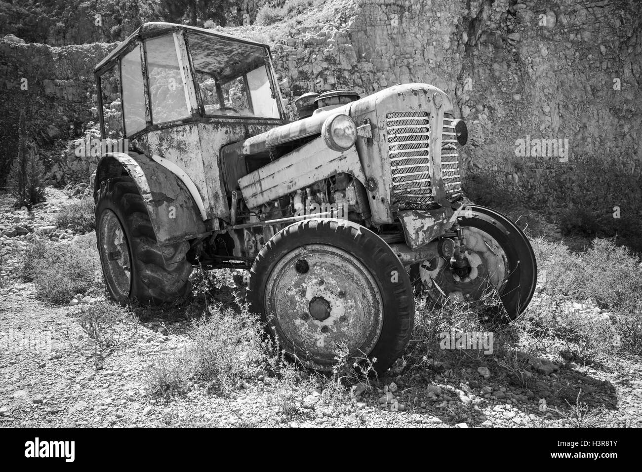 Vecchio arrugginito abbandonato il trattore si erge su erba secca. Foto in bianco e nero Foto Stock