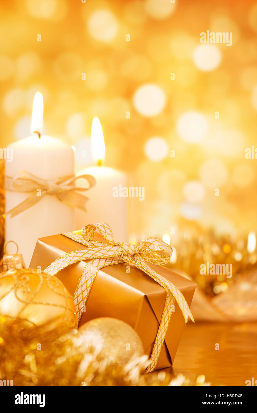 Oro baubles di Natale, candele e un regalo su un luminoso scintillante di fondo oro. Foto Stock