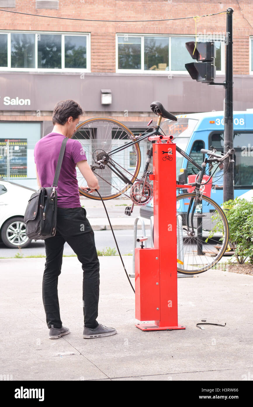 Giovane uomo pompare fino la sua moto pneumatici pneumatici a un pubblico bike stazione di riparazione stand al posto Emilie-Gamelin, Montreal city centre, Foto Stock