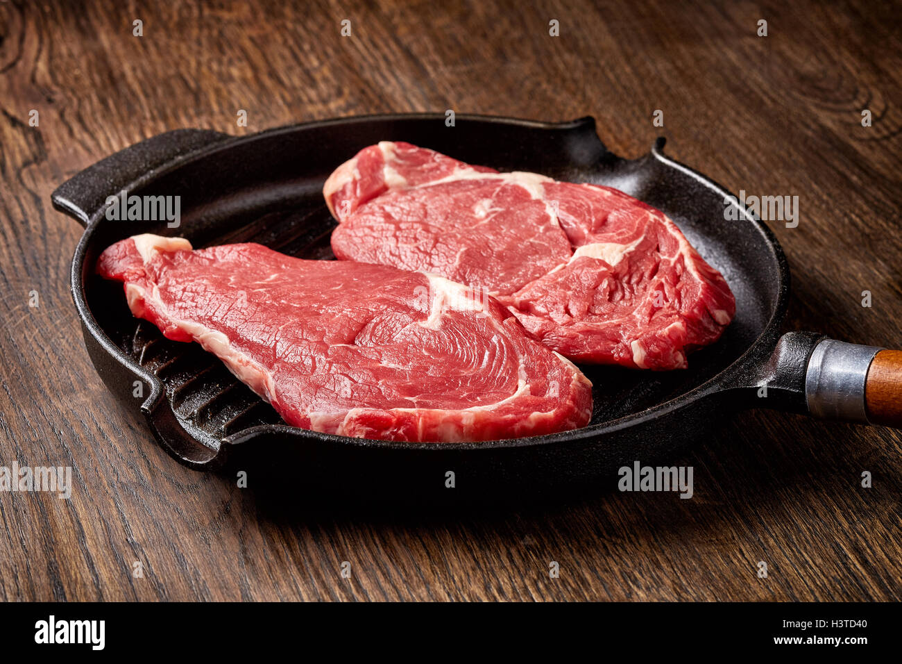 Materie bistecca in padella per grigliare su un tavolo di legno Foto Stock