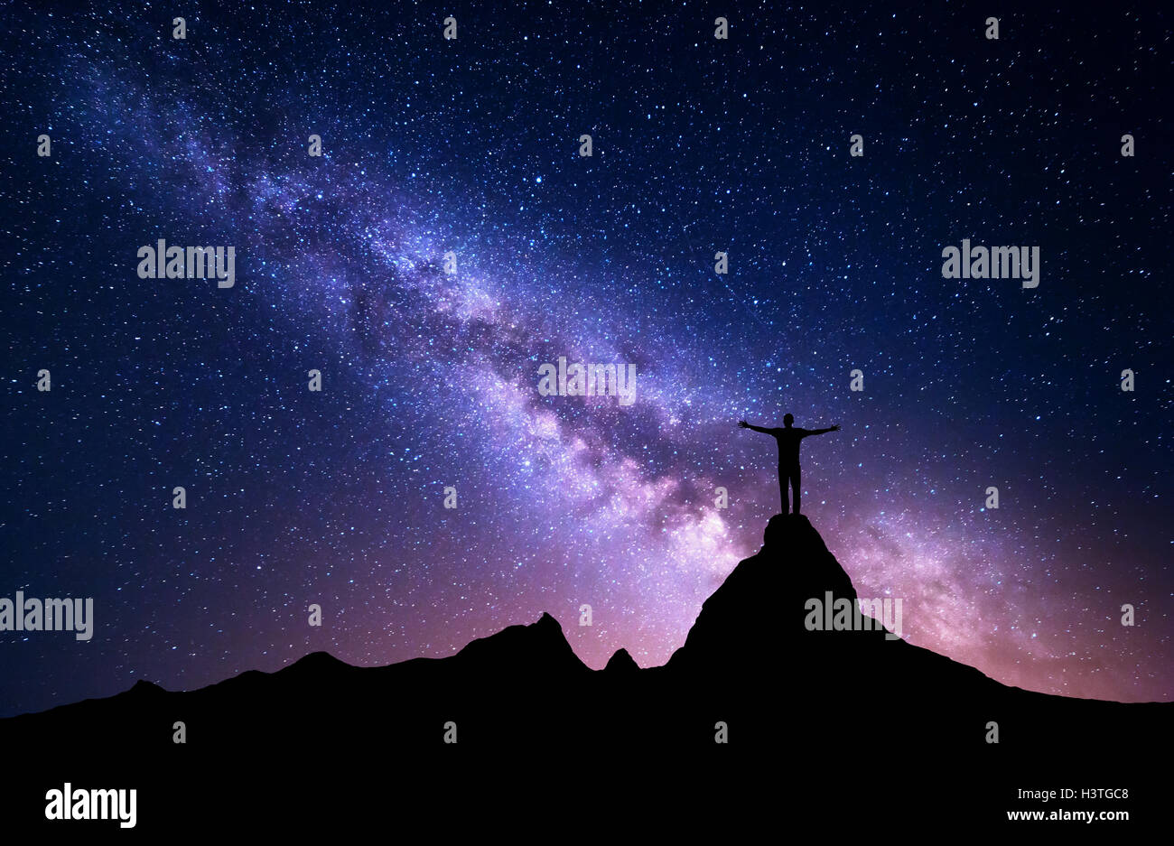 Via Lattea. Silhouette di un uomo in piedi con sollevata bracci sulla cima della montagna. Alte rocce, picco di montagna. Bella galassia. Foto Stock