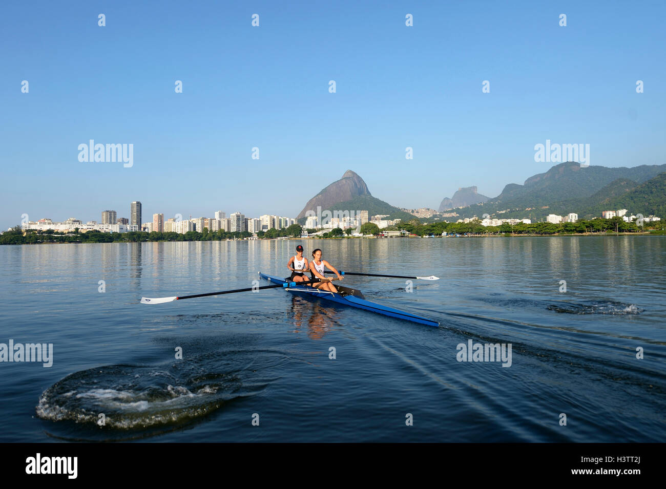 Due giovani donne che partecipano in mattina presto a remi in formazione la Lagoa Rodrigo de Freitas Lagoon, con Rio de Janeiro Foto Stock