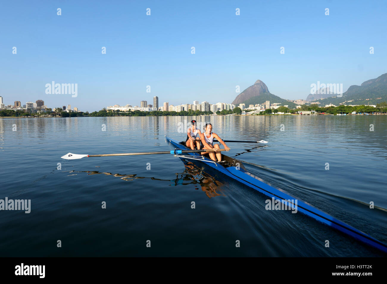 Due giovani donne che partecipano in mattina presto a remi in formazione la Lagoa Rodrigo de Freitas Lagoon, con Rio de Janeiro Foto Stock