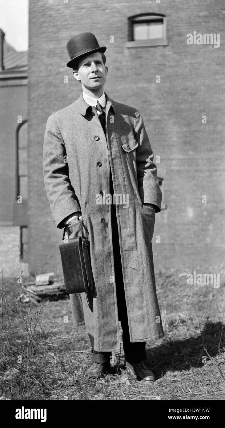 1900s 1910s PORTRAIT MAN STANDING Bowler cappello lungo cappotto di lana guardando la telecamera tenendo Custodia di pelle formato cartolina fotocamera KODAK Foto Stock