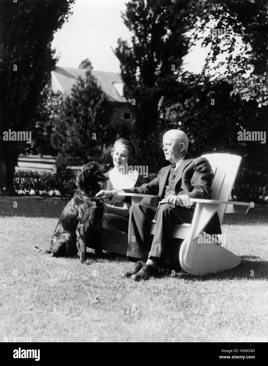 1930s uomo anziano seduto sulla sedia ADIRONDACK IN CANTIERE GIOVANE DONNA inginocchiato accanto a lui con setter irlandese cane Foto Stock