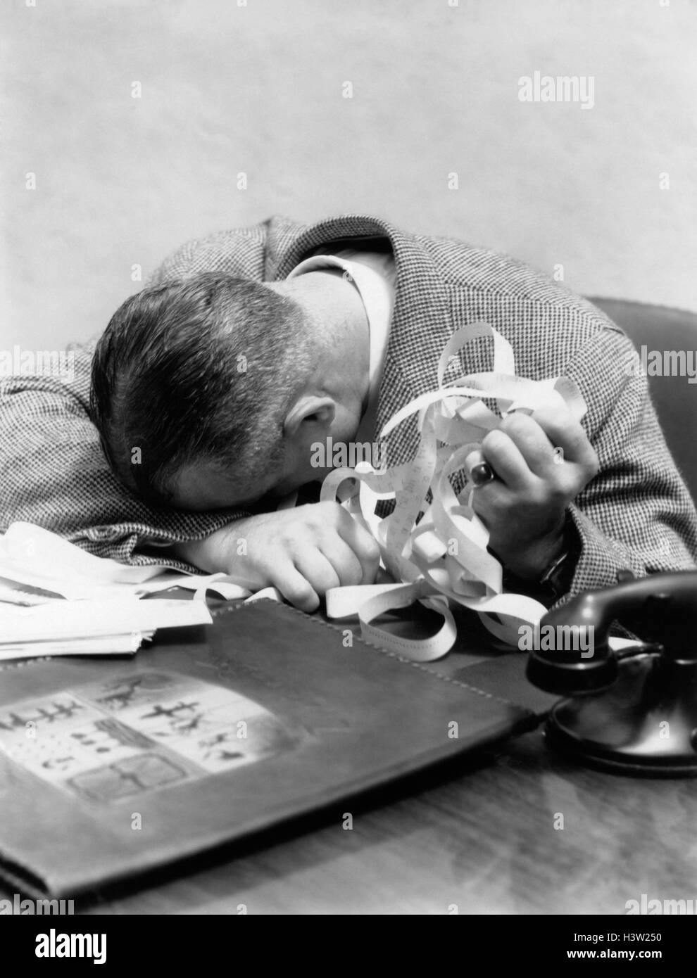 1930s 1940s uomo con la testa in giù sulla scrivania e Stock Ticker tape IN MANO Foto Stock