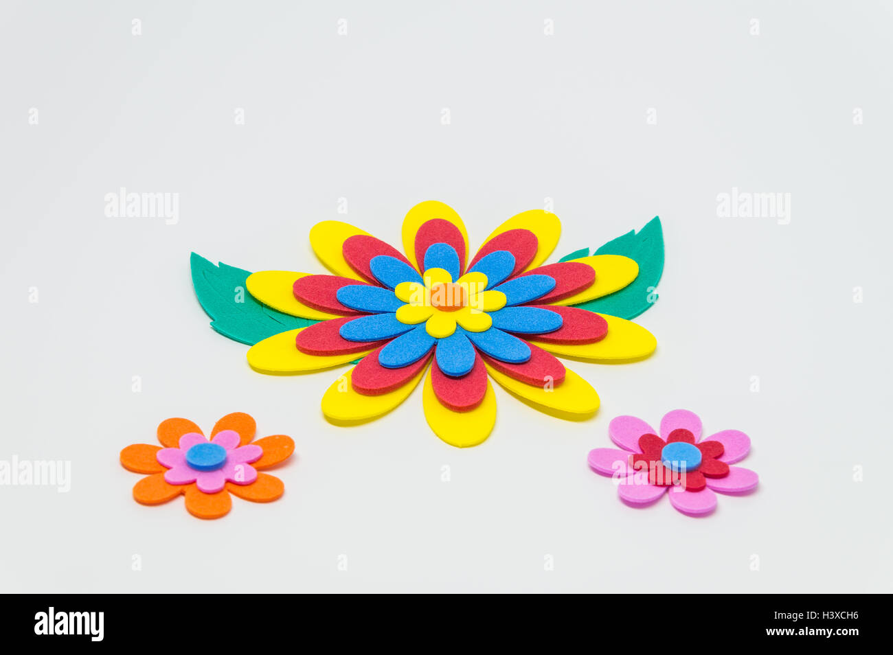 Schiuma di coloratissimi fiori artigianali con foglia verde su sfondo bianco e messa a fuoco selettiva Foto Stock