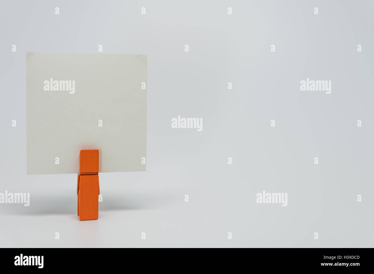 Pezzo di carta Memo serrato da orange clip in legno con sfondo bianco e messa a fuoco selettiva Foto Stock