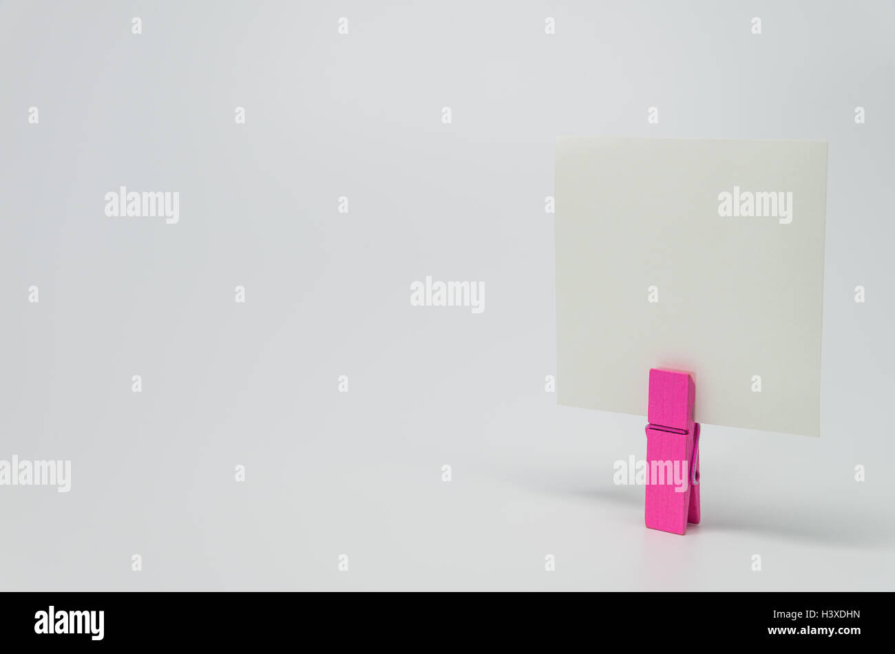 Pezzo di carta Memo serrato da rosa clip in legno con sfondo bianco e messa a fuoco selettiva Foto Stock