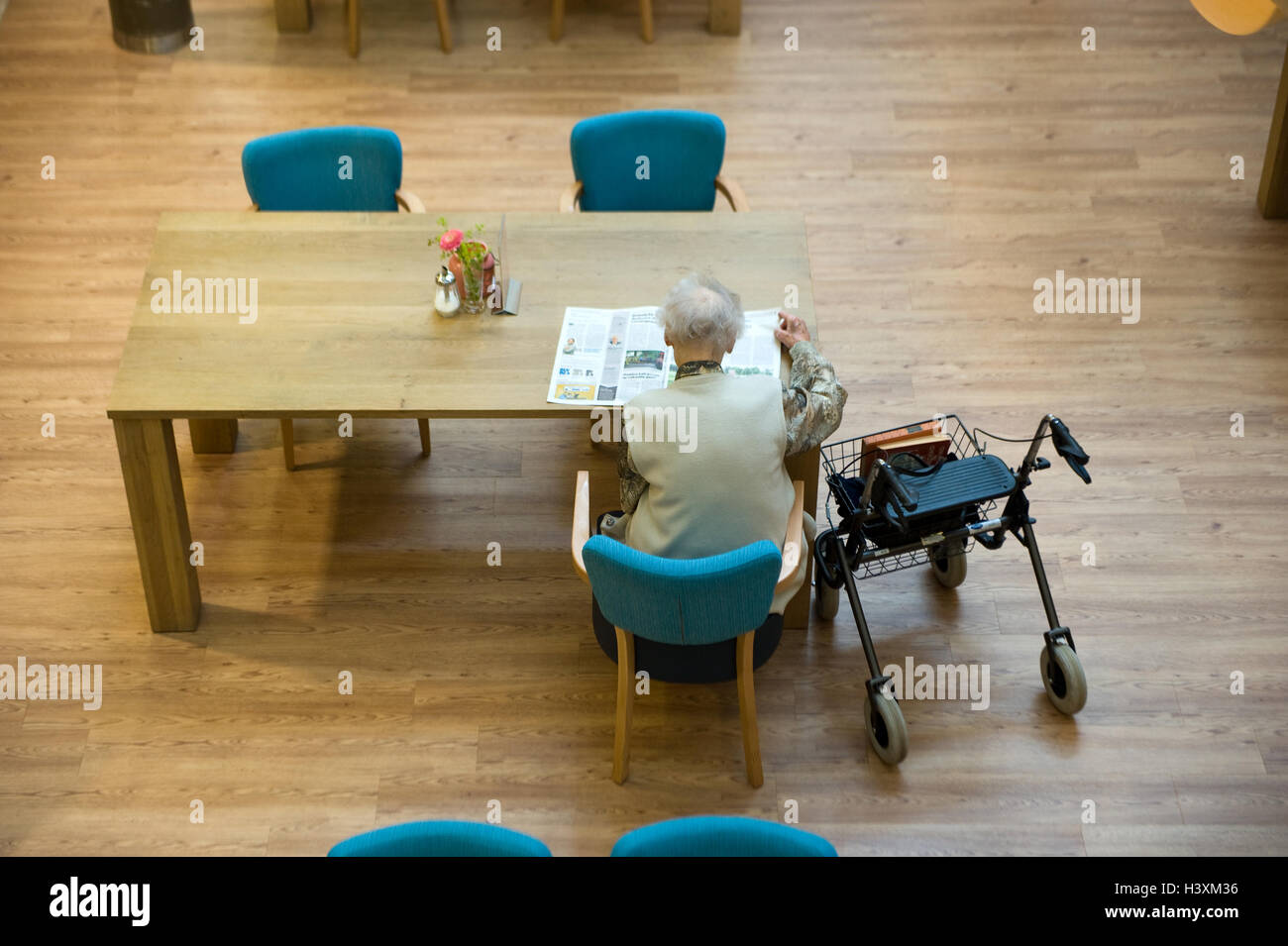 ALMELO, Paesi Bassi - 14 giugno 2016: Una donna anziana sta leggendo un giornale sul tavolo di una casa anziani. Foto Stock