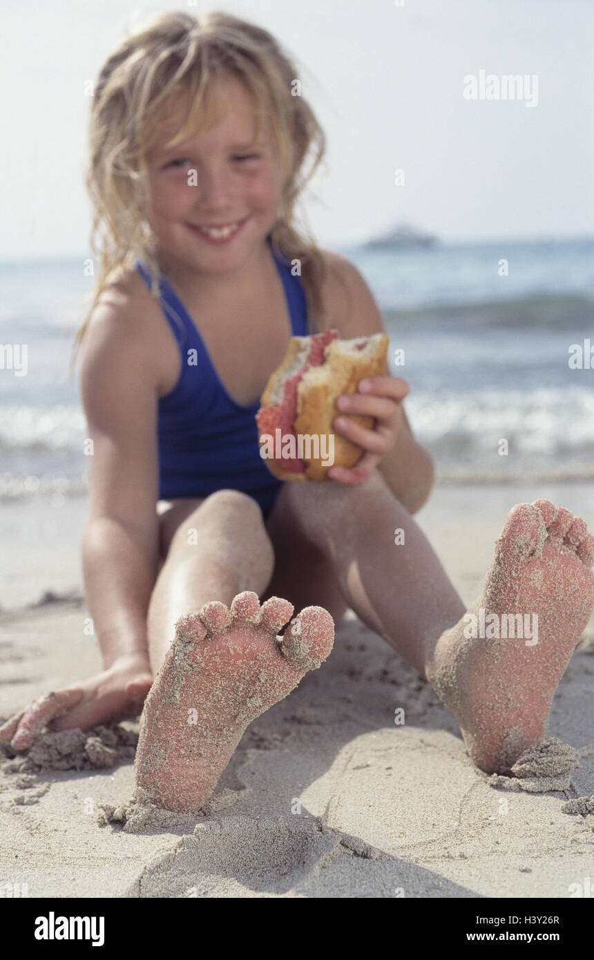 Spiaggia di sabbia, ragazza, pane, felice, esterno, mare, estate, spiaggia, sabbia, vacanza, vacanze, tempo libero e l'infanzia, bambino, 8 anni, Felice, costume da bagno, costumi da bagno, intermeal, libri, sandwich, giocare sento Foto Stock