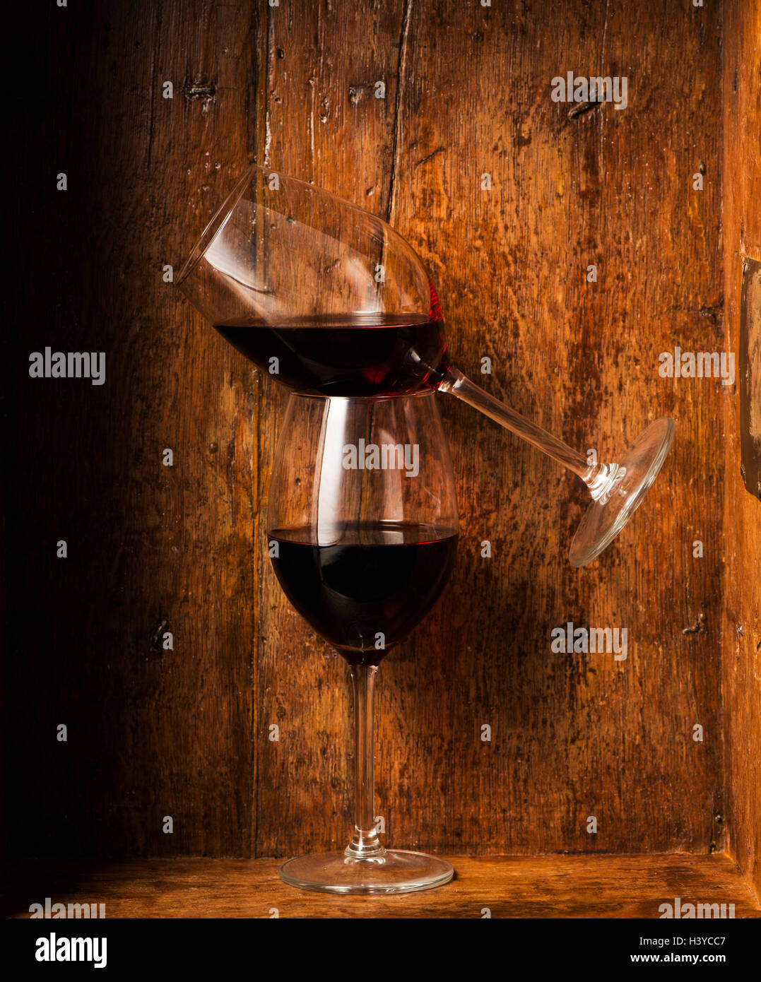 Due bicchieri di vino rosso. Uno è in equilibrio su altri. In legno rustico sfondo. Concetto di alcol e di equilibrio. Foto Stock