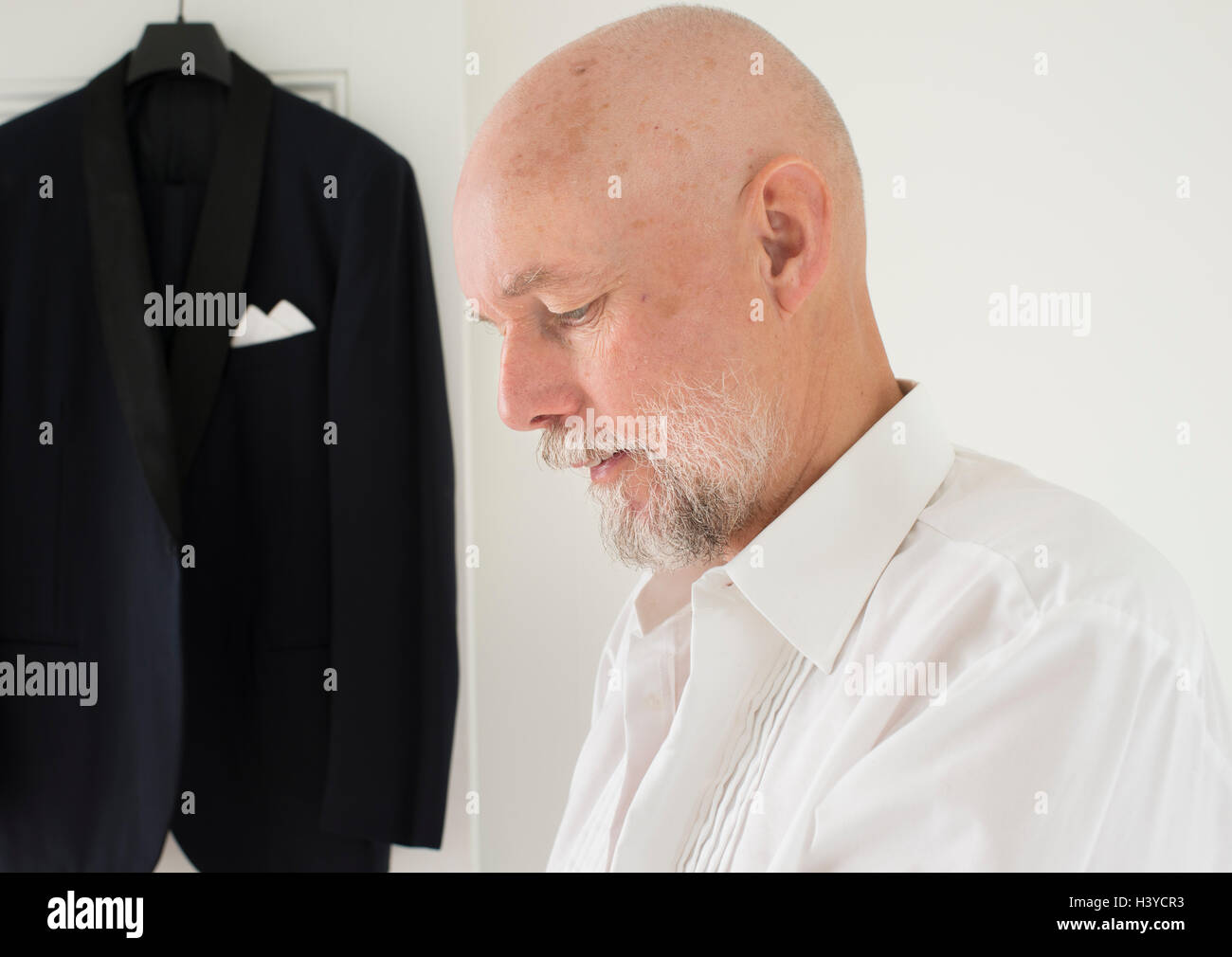 Il vecchio uomo di mettere su vestiti a casa, cena giacca appesa in background. Momento di uno stile di vita attivo di pensionamento. Foto Stock