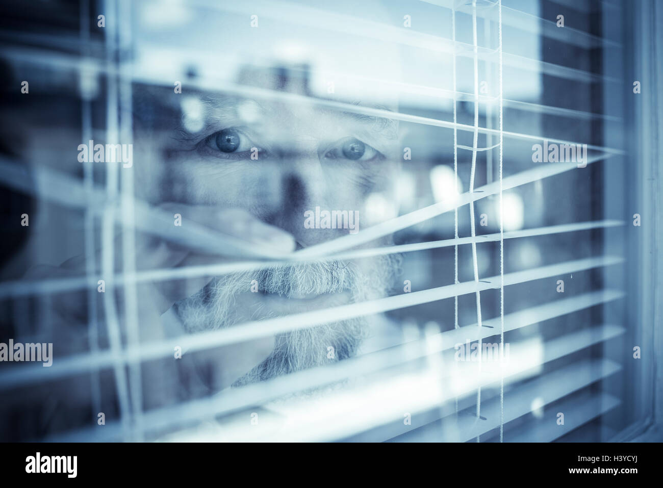 Il vecchio uomo guardando fuori della finestra attraverso le persiane. Concetto di visione e la zona di sorveglianza. Sentirsi insicuro nella vostra casa. Foto Stock