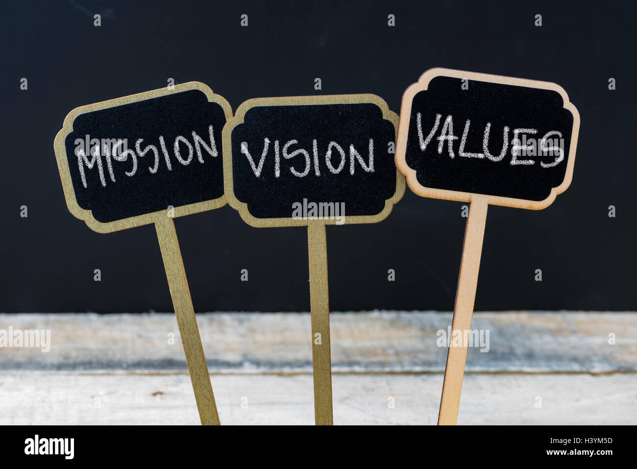 Messaggio di Business Missione, visione, valori scritti con il gesso su legno mini blackboard etichette, lavagna sfocati e tavola di legno in background Foto Stock
