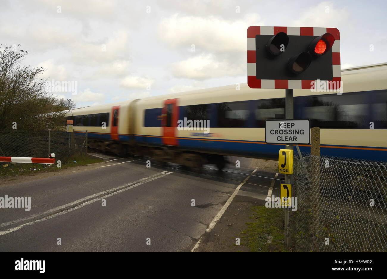 'Level crossing' attraversamento ferroviario, treno andando su un passaggio a livello ferroviario, ferrovia strada incrocio, passaggio a livello con barriere, REGNO UNITO Foto Stock