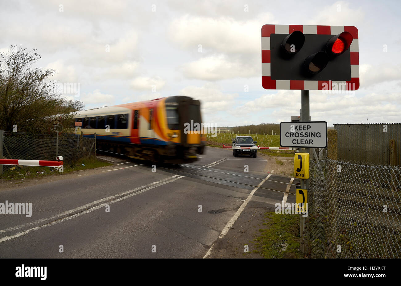 'Level crossing' attraversamento ferroviario, treno andando su un passaggio a livello ferroviario, ferrovia strada incrocio, passaggio a livello con barriere, REGNO UNITO Foto Stock