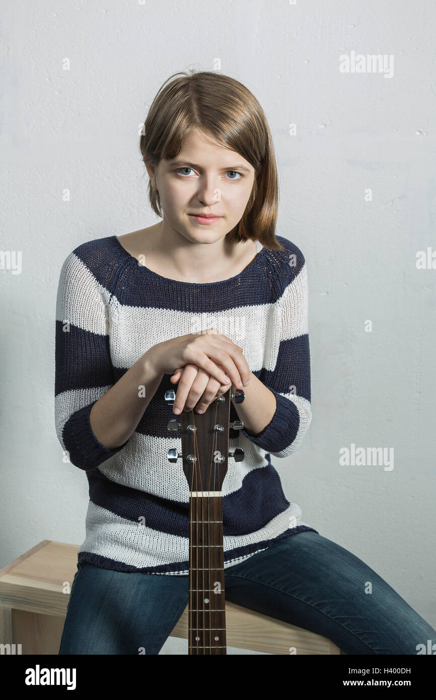 Ritratto di adolescente sorridente tenendo la chitarra mentre è seduto su un banco di lavoro contro la parete Foto Stock