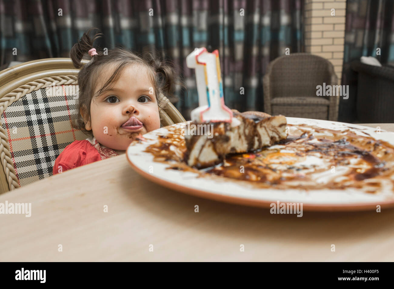 Ritratto di ragazza carina spuntavano lingua con faccia disordinato mentre avente torta di compleanno a tavola Foto Stock