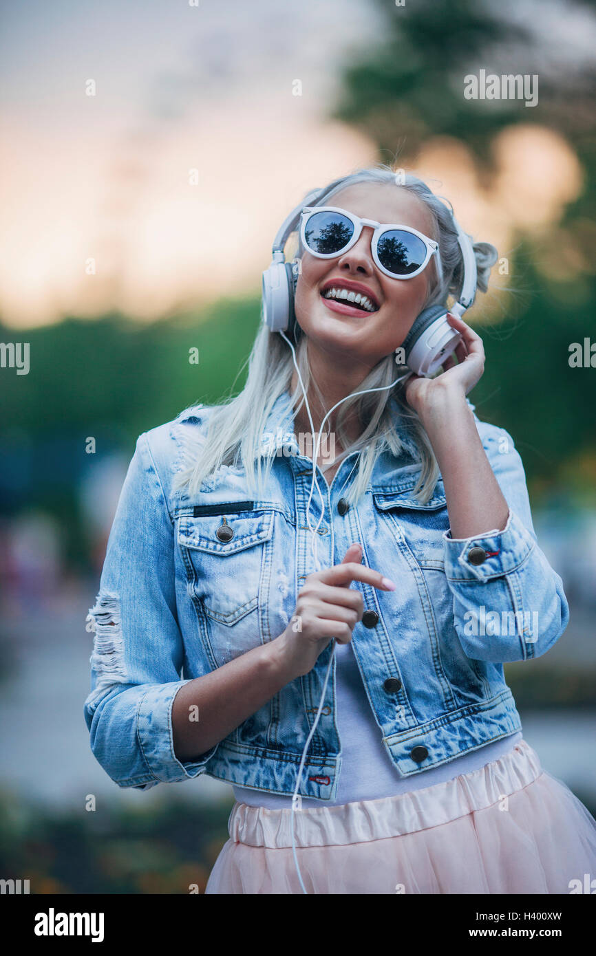 Felice di moda donna che indossa gli occhiali da sole mentre si ascolta la musica attraverso le cuffie Foto Stock