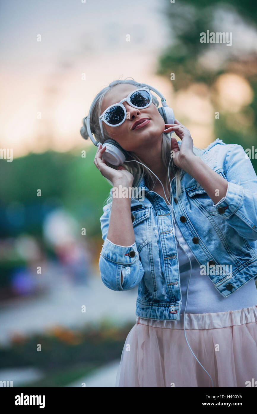 Moda giovane donna che indossa gli occhiali da sole mentre si ascolta la musica attraverso le cuffie Foto Stock